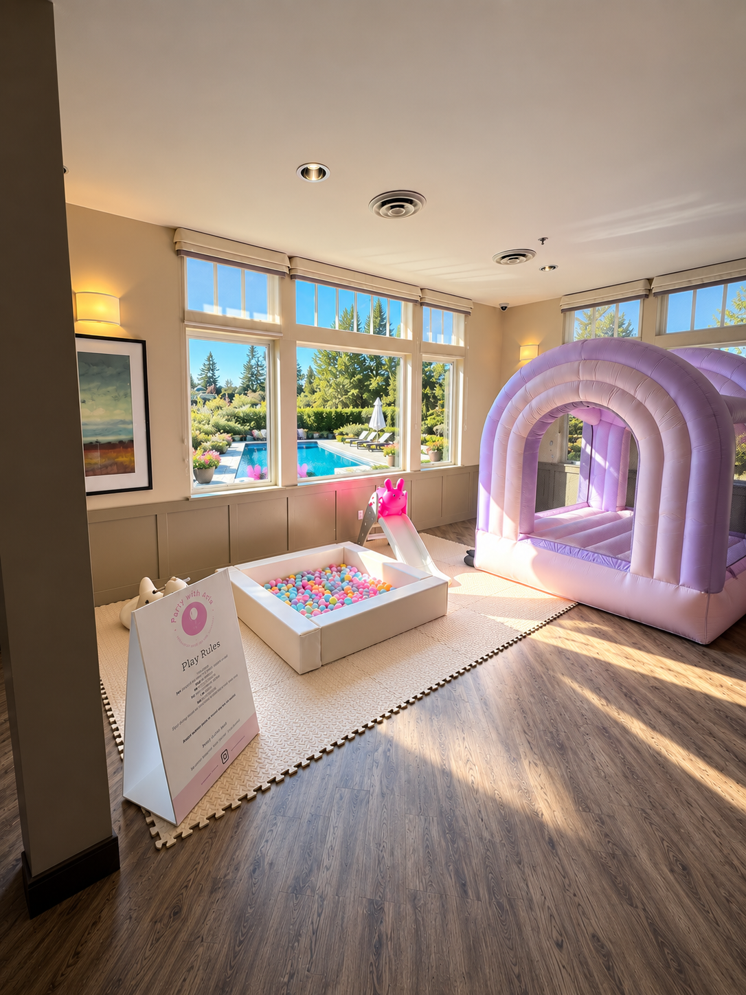 A Party with Aria play setup with a white ball pit, pastel balls, slide, mats, bounce castle and the original Play Rules sign.